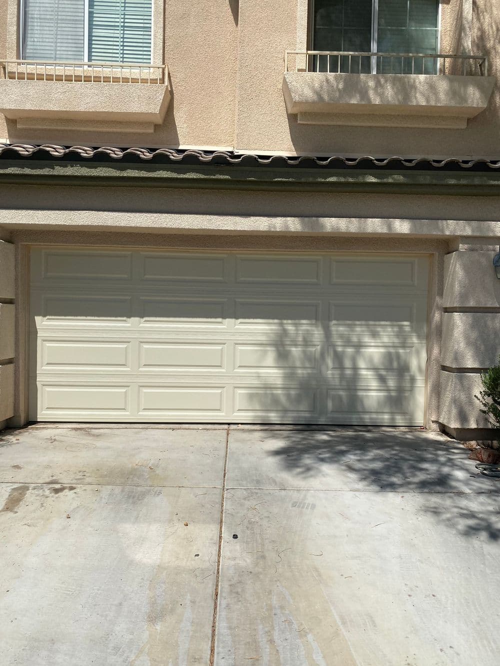 Cream-colored garage door with multiple panels, set against a beige house facade.
